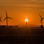 The sun sets behind wind turbines